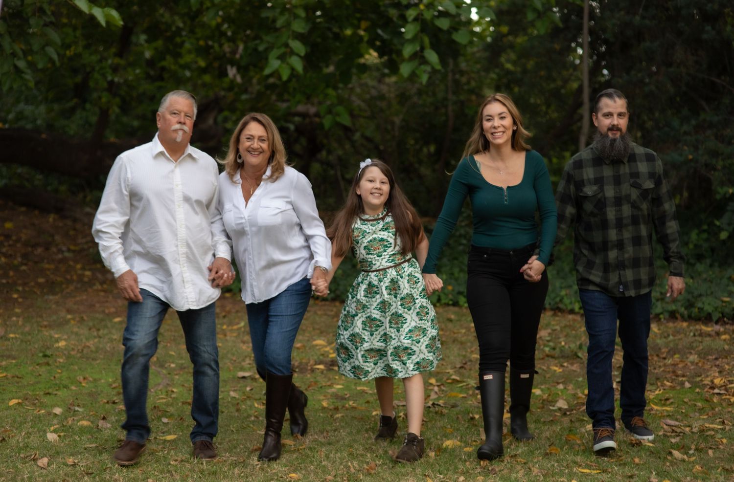 Five people walking together outdoors in casual attire against a green background.