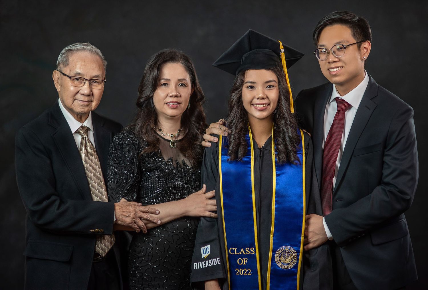 A formal graduation portrait with academic regalia against a dark background.