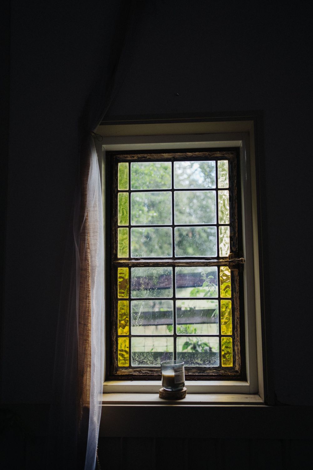 A vintage window with yellow stained glass panels framing a tranquil garden view.