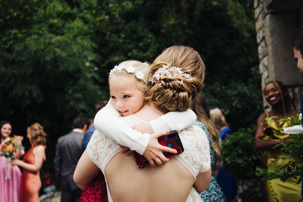 A tender embrace during a sun-dappled outdoor wedding ceremony with guests looking on.