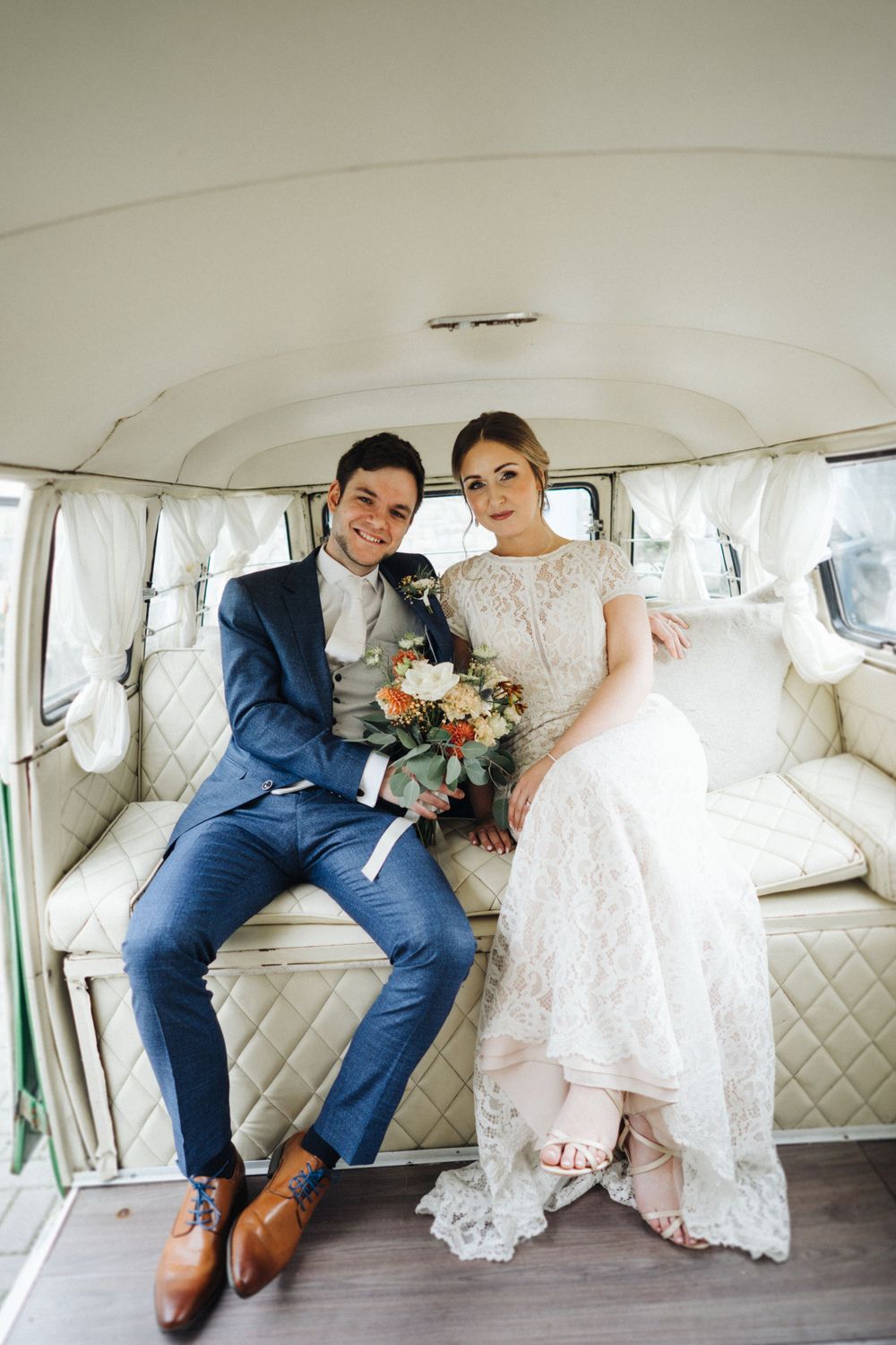 A couple in wedding attire poses inside a vintage white van with quilted interior seating.