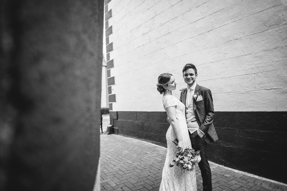 Black and white portrait of newlyweds standing against a brick wall.