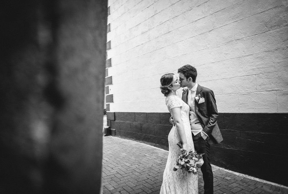 Artistic black and white shot of a wedding couple by a modern building wall.