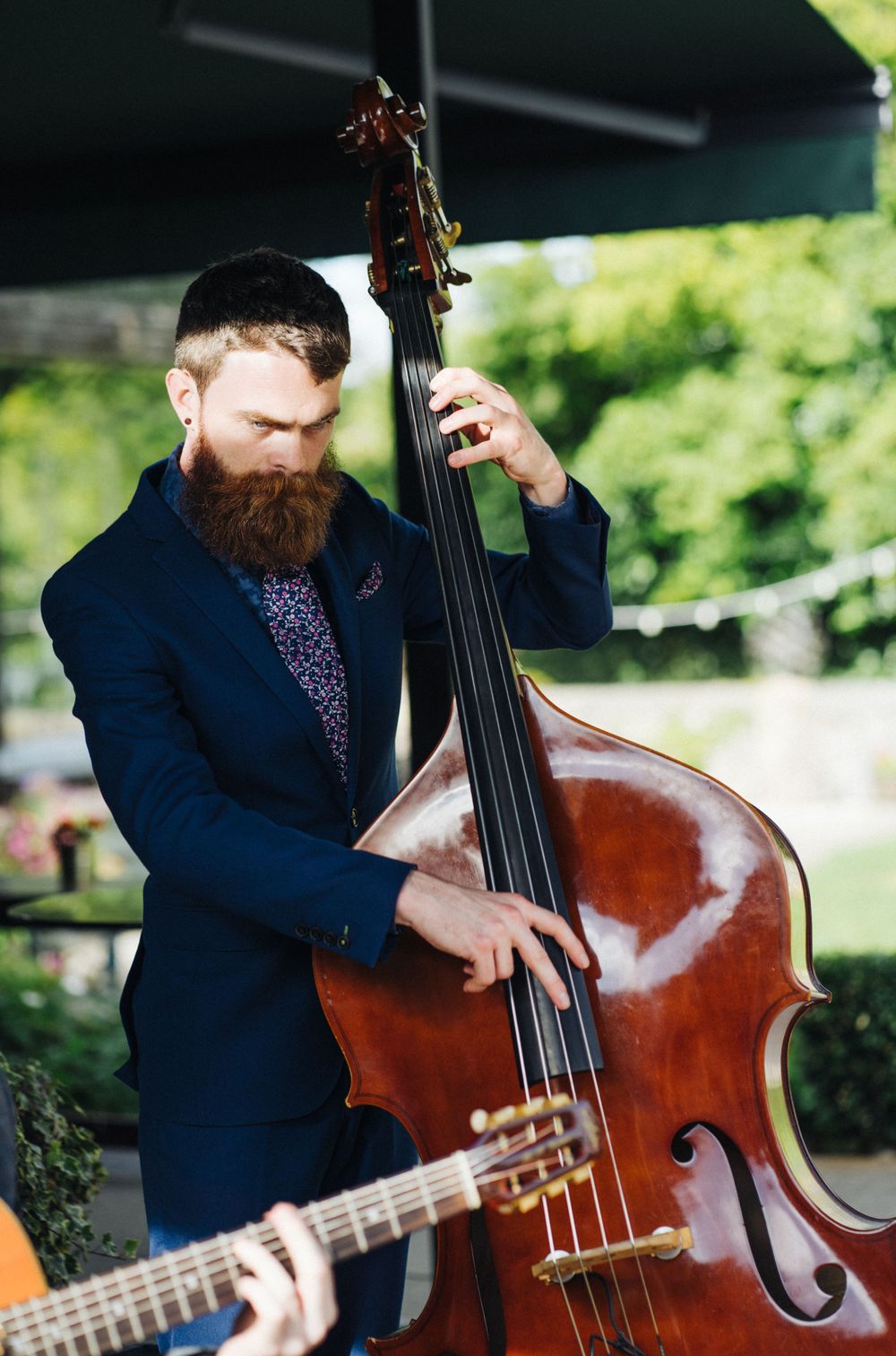 Musician performing with upright bass at outdoor event wearing navy suit with floral tie.