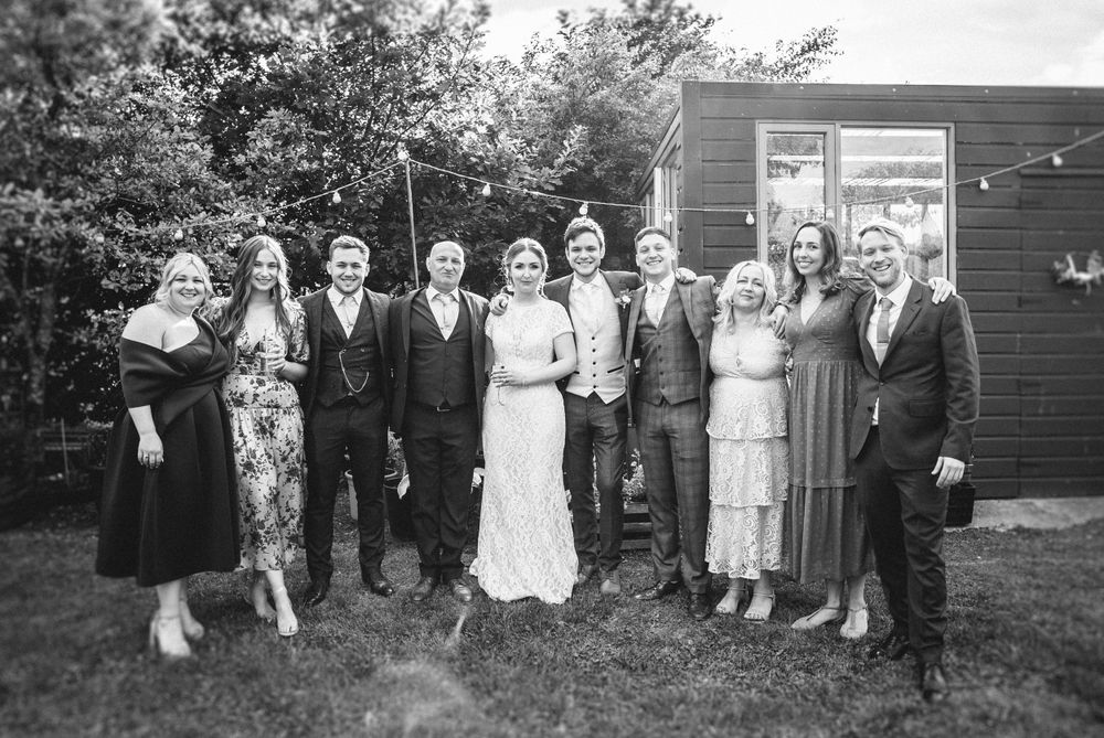 Vintage black and white photo of well-dressed wedding party posing outside wooden building.