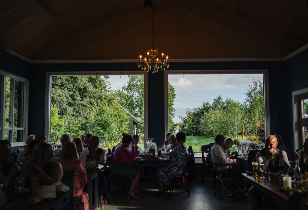 Guests enjoy a meal in a bright dining room with large windows overlooking lush greenery and gardens.