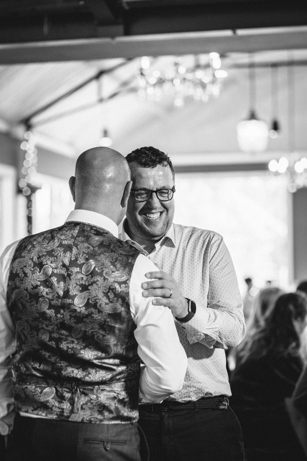 Two people share an intimate dance moment under sparkling chandeliers at an indoor reception.