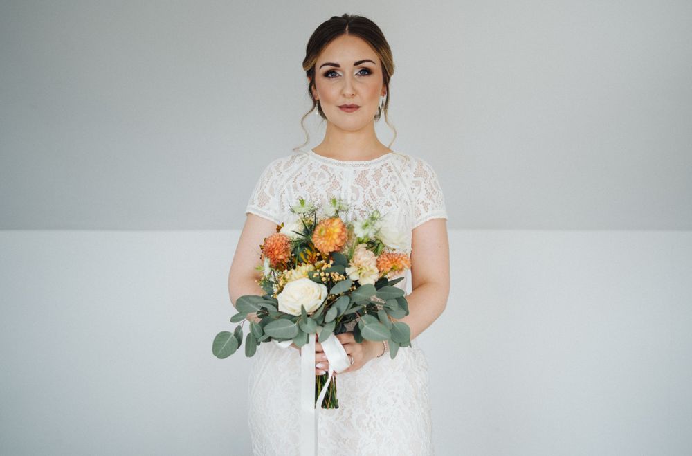 An elegant bouquet of peach and cream flowers with eucalyptus leaves held against a white background.
