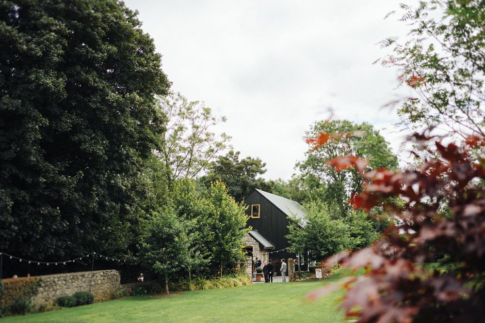 A scenic view of a countryside house with lush gardens and trees under an overcast sky.