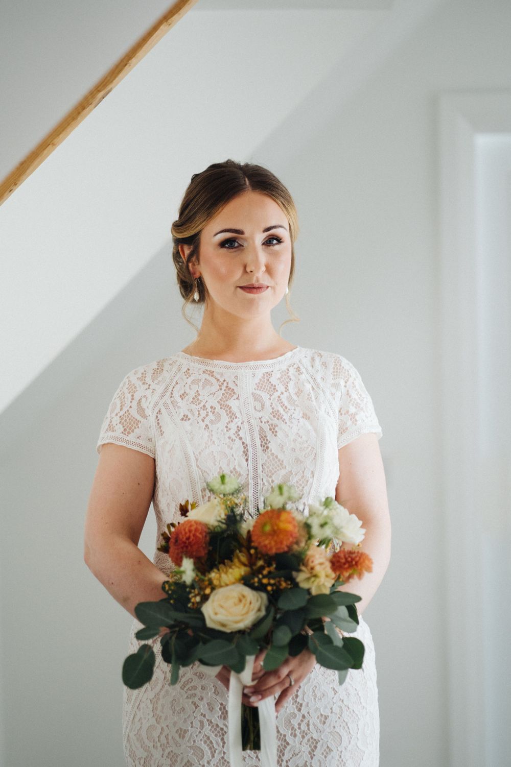 A person in a white lace wedding dress holds a vibrant bouquet with orange and cream flowers.