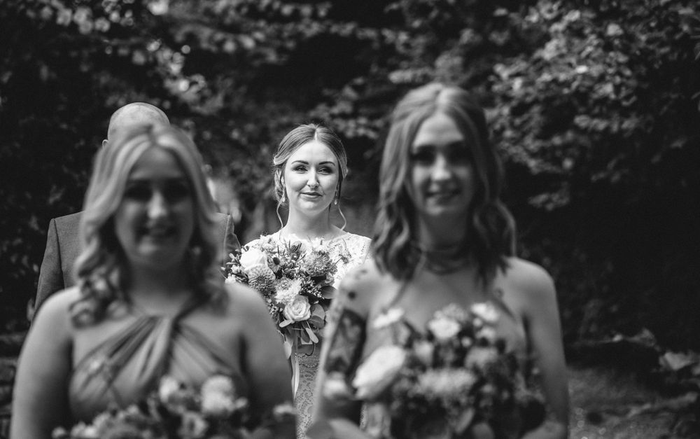 A formal processional walks down an indoor aisle lined with wedding guests.