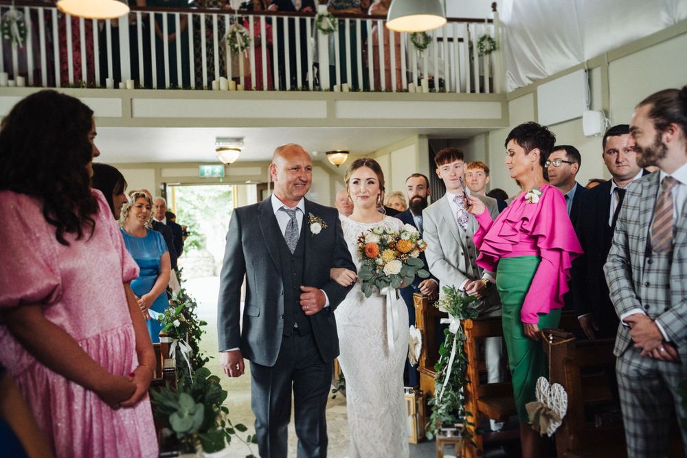 A black and white photo captures a wedding processional with guests looking on.