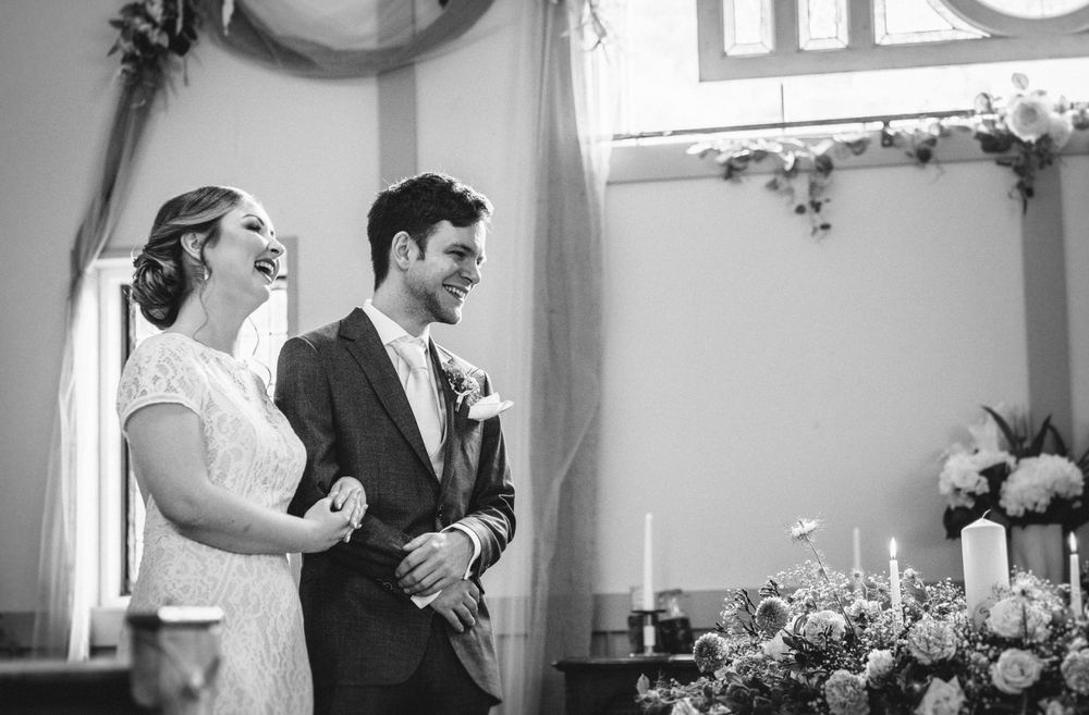 A black and white photograph of a joyful moment during a wedding ceremony under decorative lighting.
