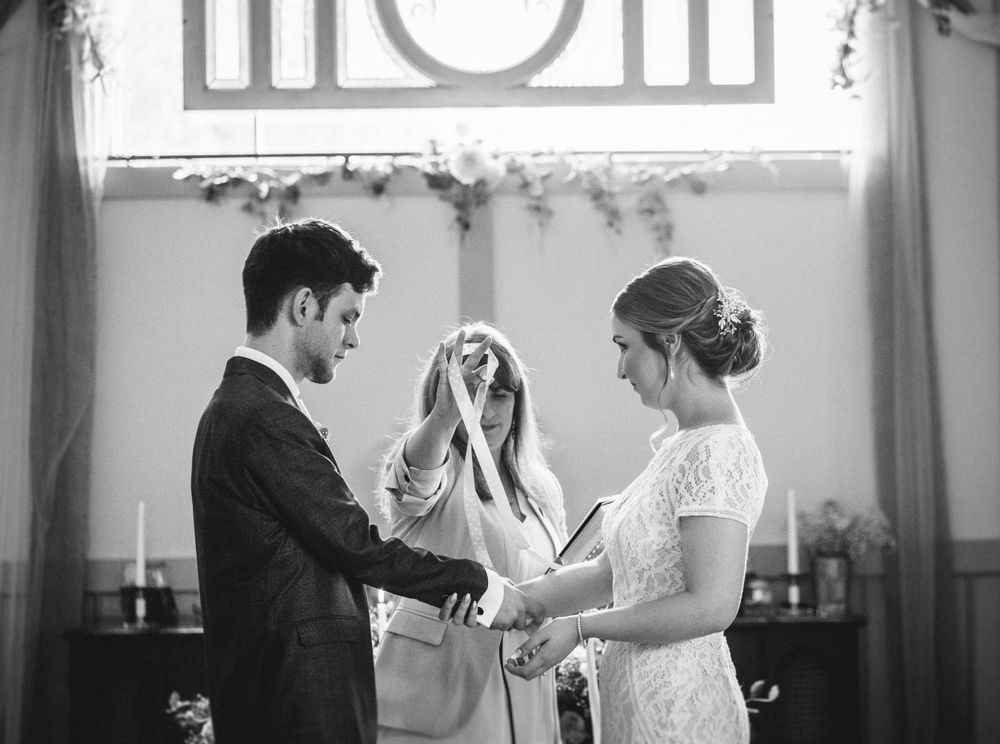 A black and white image capturing an intimate wedding ceremony moment with floral decorations.
