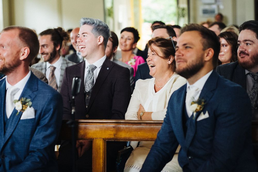 Wedding guests in formal attire sharing laughter during the ceremony.
