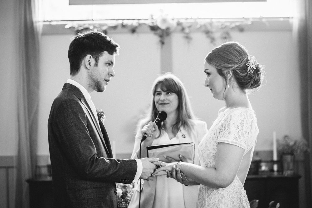 A black and white photo of an intimate wedding ceremony in a sunlit room.
