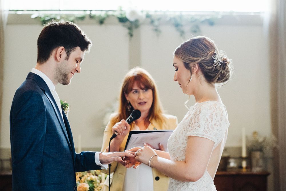 A warm-toned wedding ceremony photo showing the exchange of rings during the service.