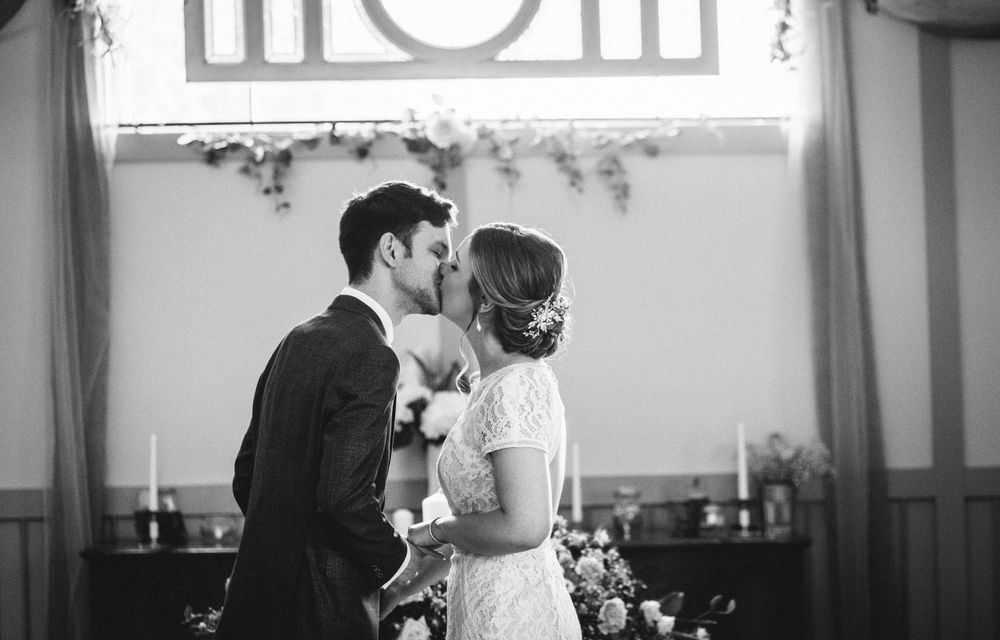 A black and white photo capturing a tender wedding ceremony moment beneath a window.