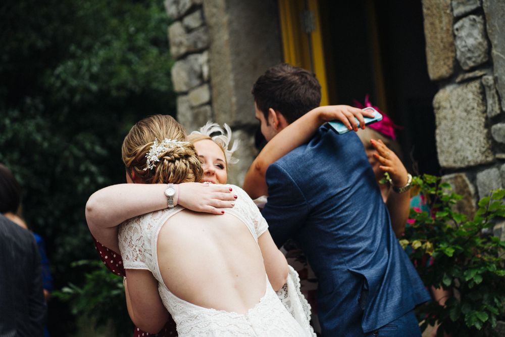 Wedding guests embrace during outdoor celebrations near stone architecture.
