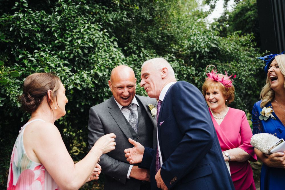 Wedding guests share laughter and conversation during an outdoor garden reception.