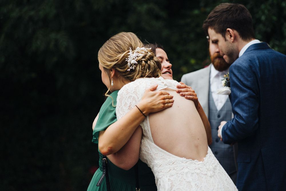 Wedding party members share an emotional embrace outdoors against a natural green backdrop.