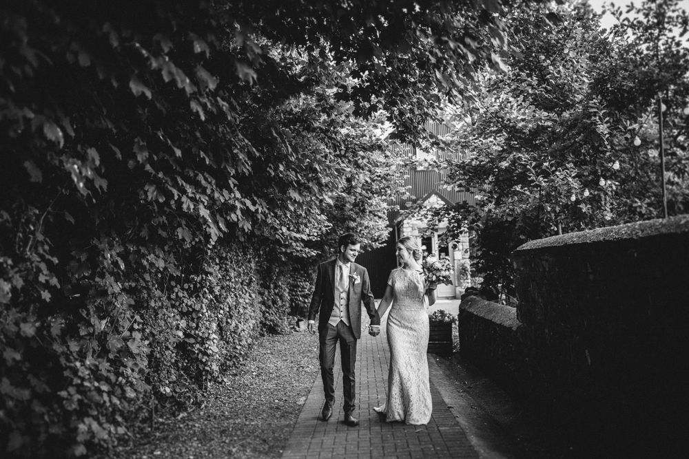 Black and white photo of couple walking together on tree-lined path.
