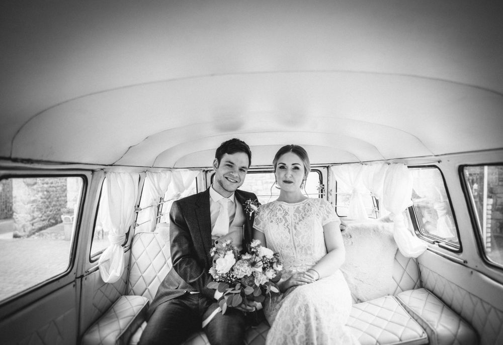 A couple sits together holding flowers inside a classic vintage van in black and white.