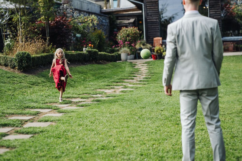 Child in red dress running along garden stepping stones while adult watches.