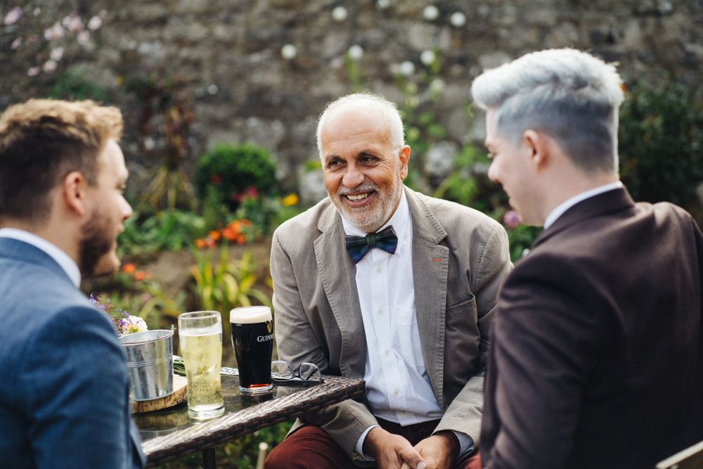 Three guests engaged in conversation over drinks at an outdoor wedding reception.