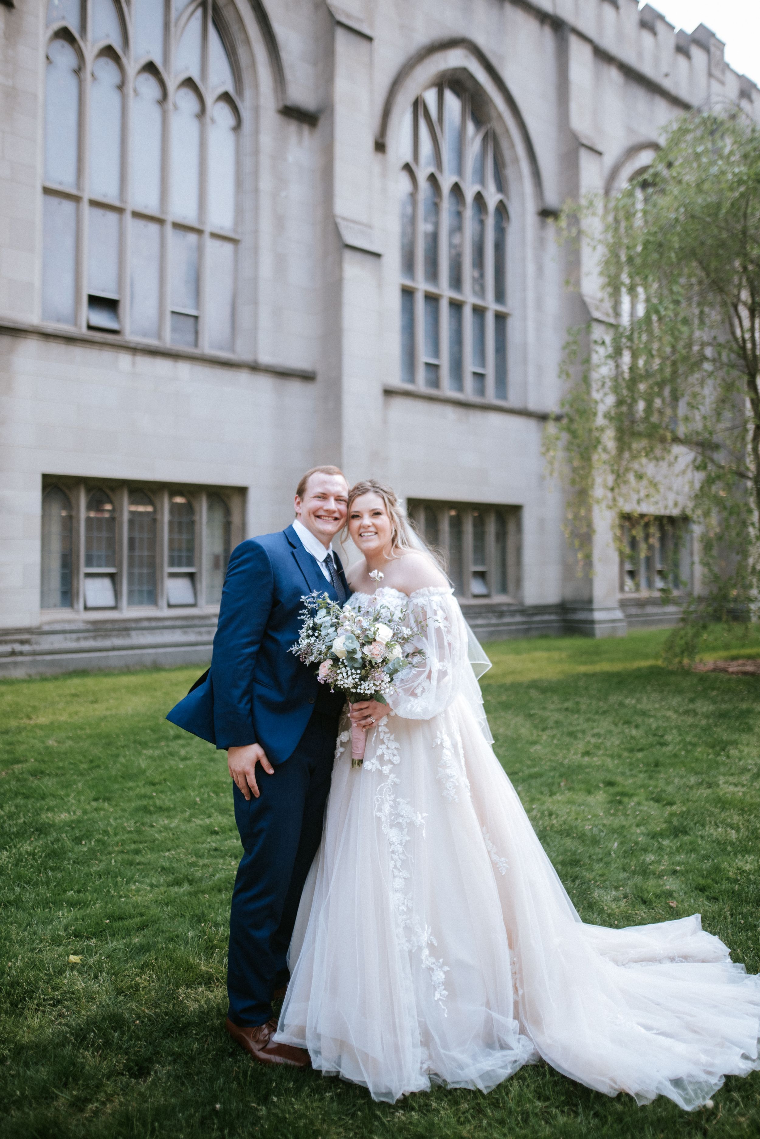 Wedding couple poses with elegant bouquet outside gothic church architecture.