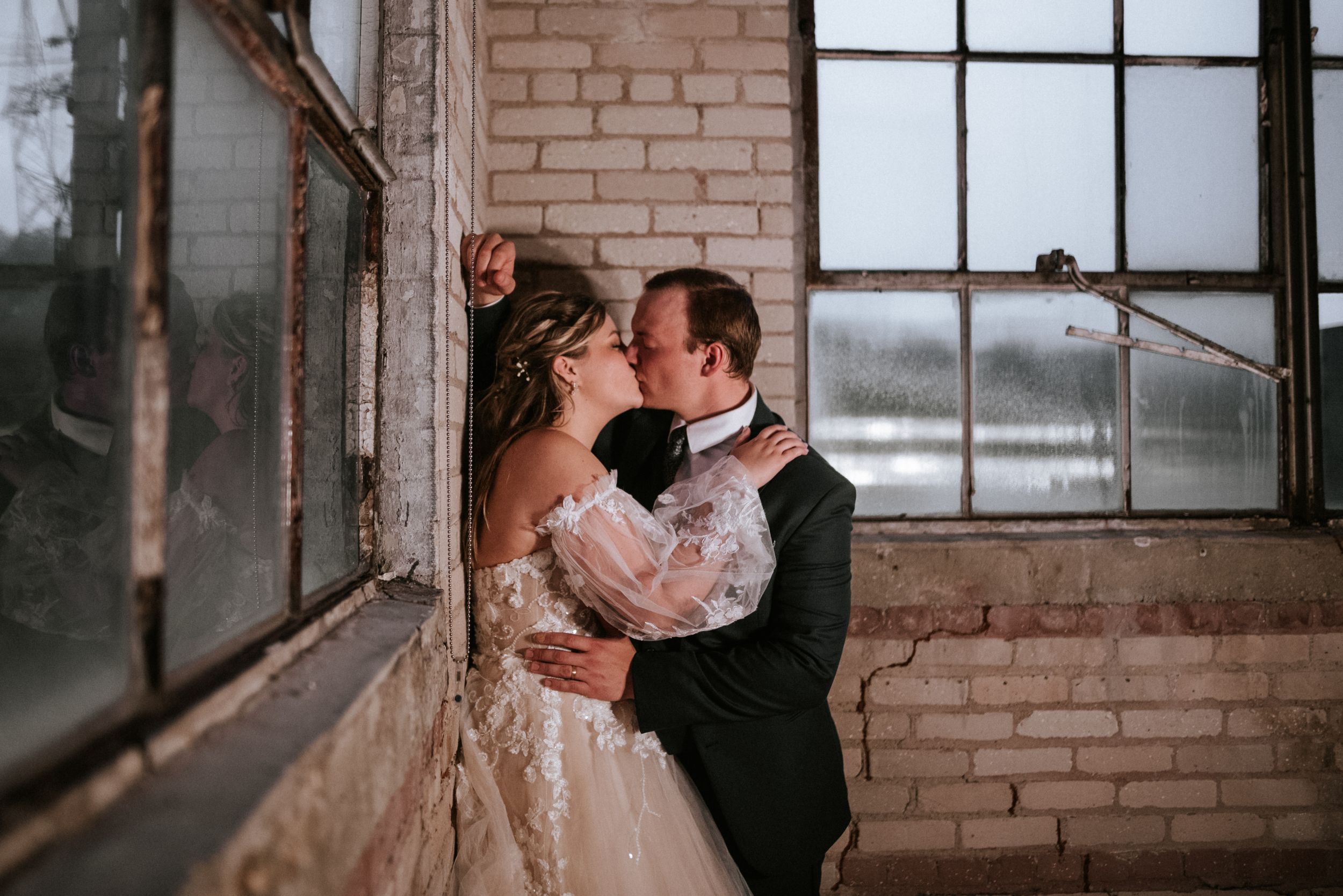 An intimate wedding moment captured in a rustic brick warehouse with large vintage windows.