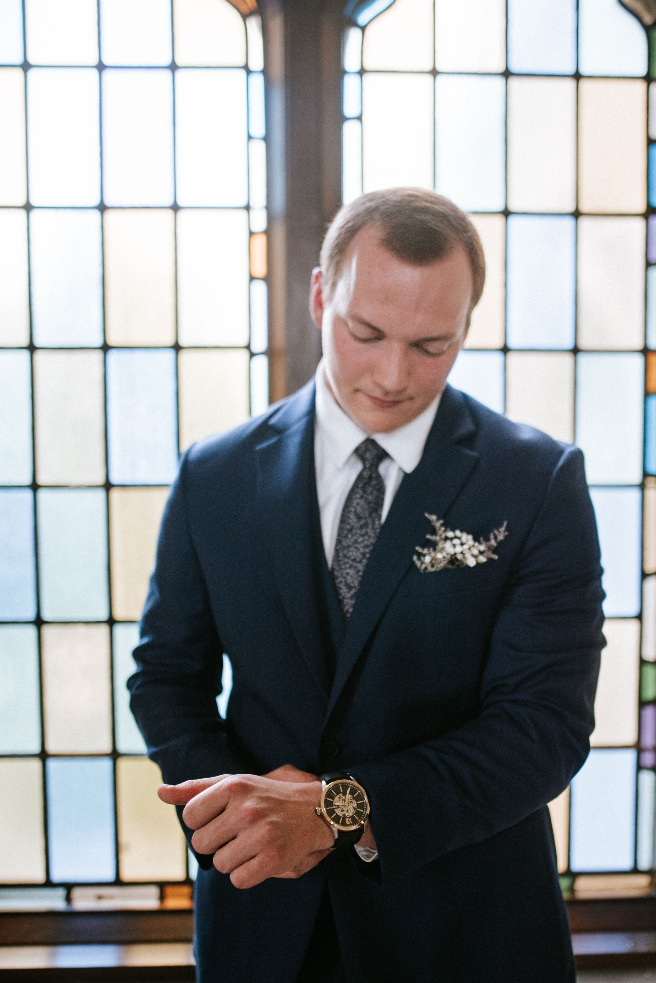 Formal portrait of a groom in navy suit against stained glass windows.