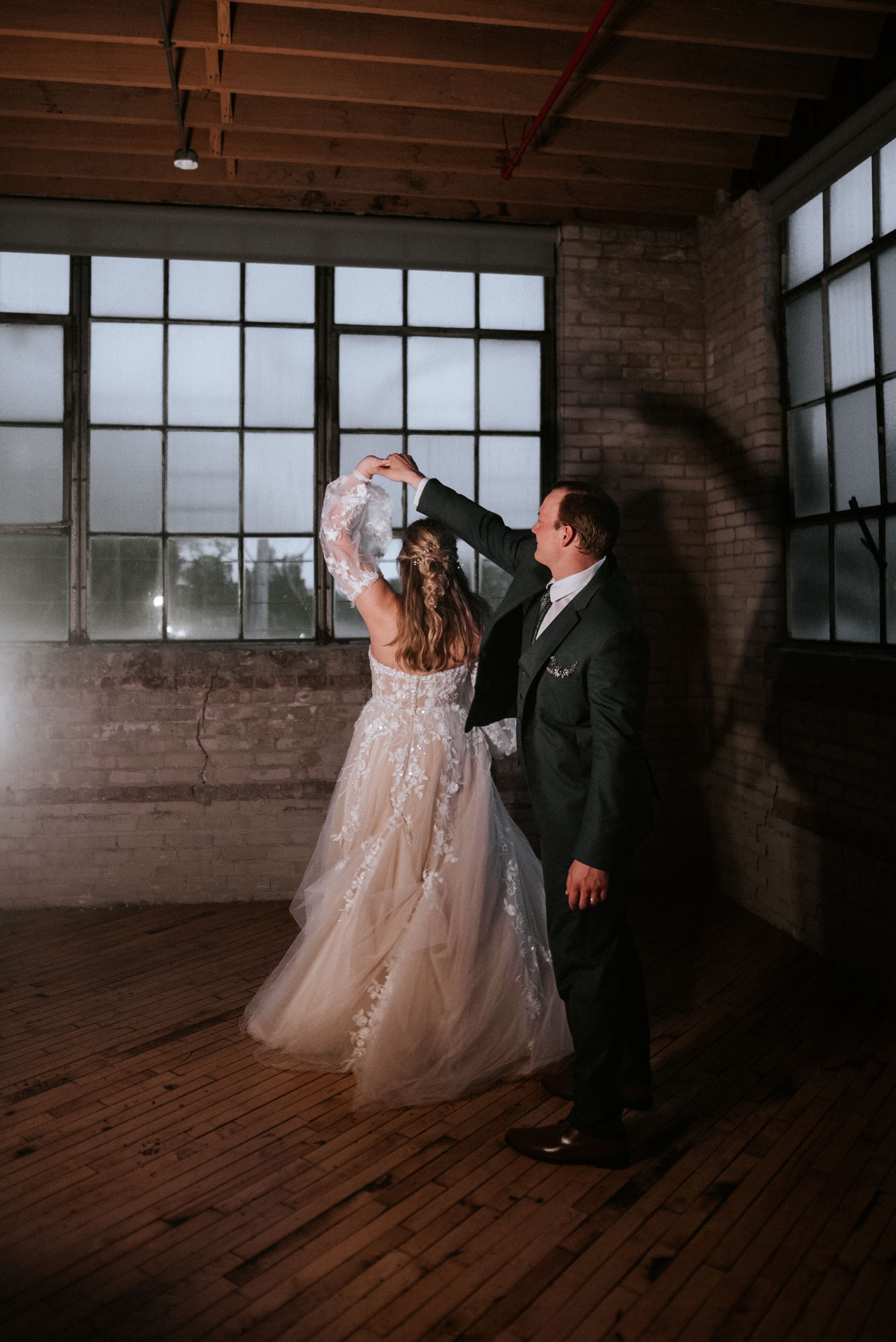 A dancing couple in wedding attire inside an industrial space with exposed brick and wooden floors.