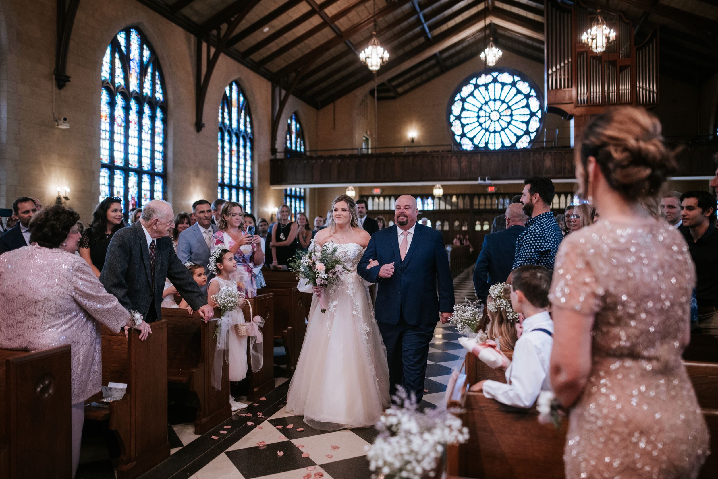 Wedding ceremony in a beautiful church with gothic windows and wooden beams featuring guests in formal attire.