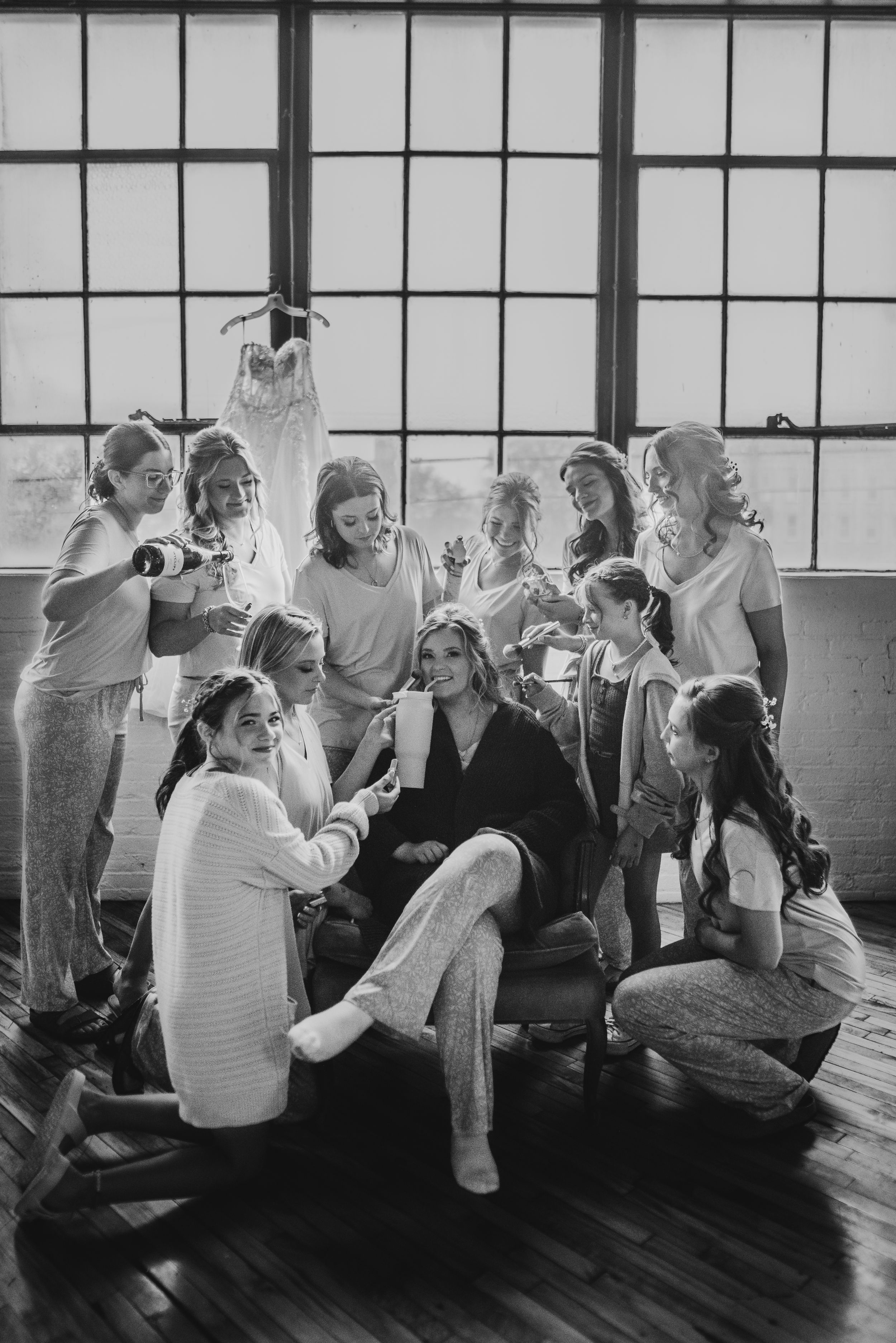 Black and white photo of bridal party getting ready in loft space with hanging dress.