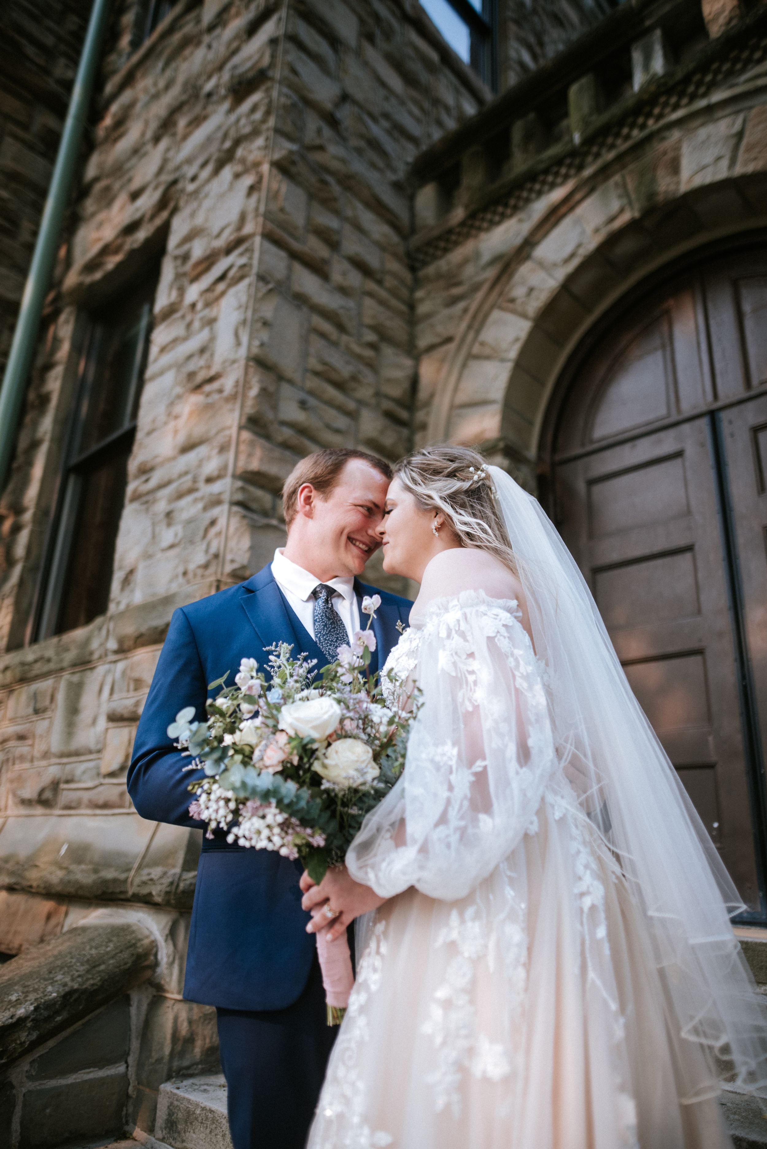 Intimate wedding portrait of couple against stone church architecture.