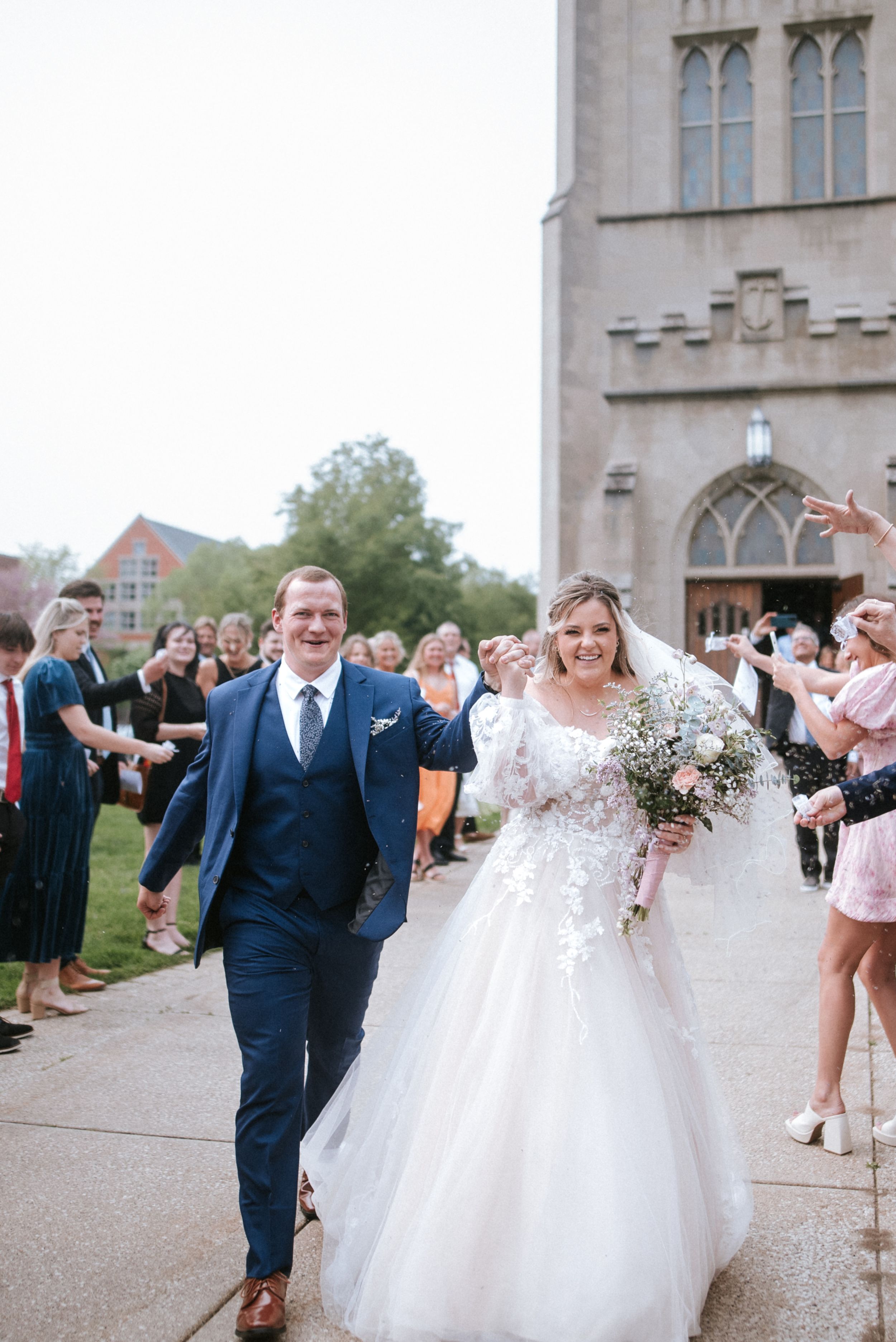 A newlywed couple exits a gothic stone church while guests line the walkway.