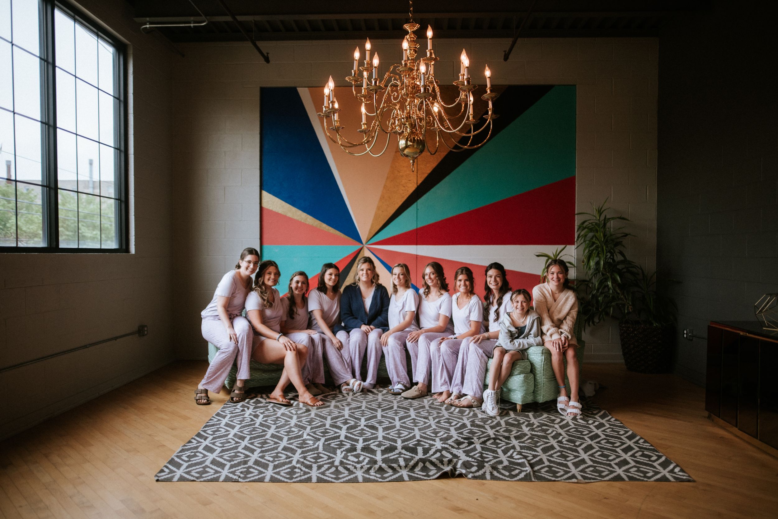 Wedding party seated together under a chandelier with colorful geometric wall art.