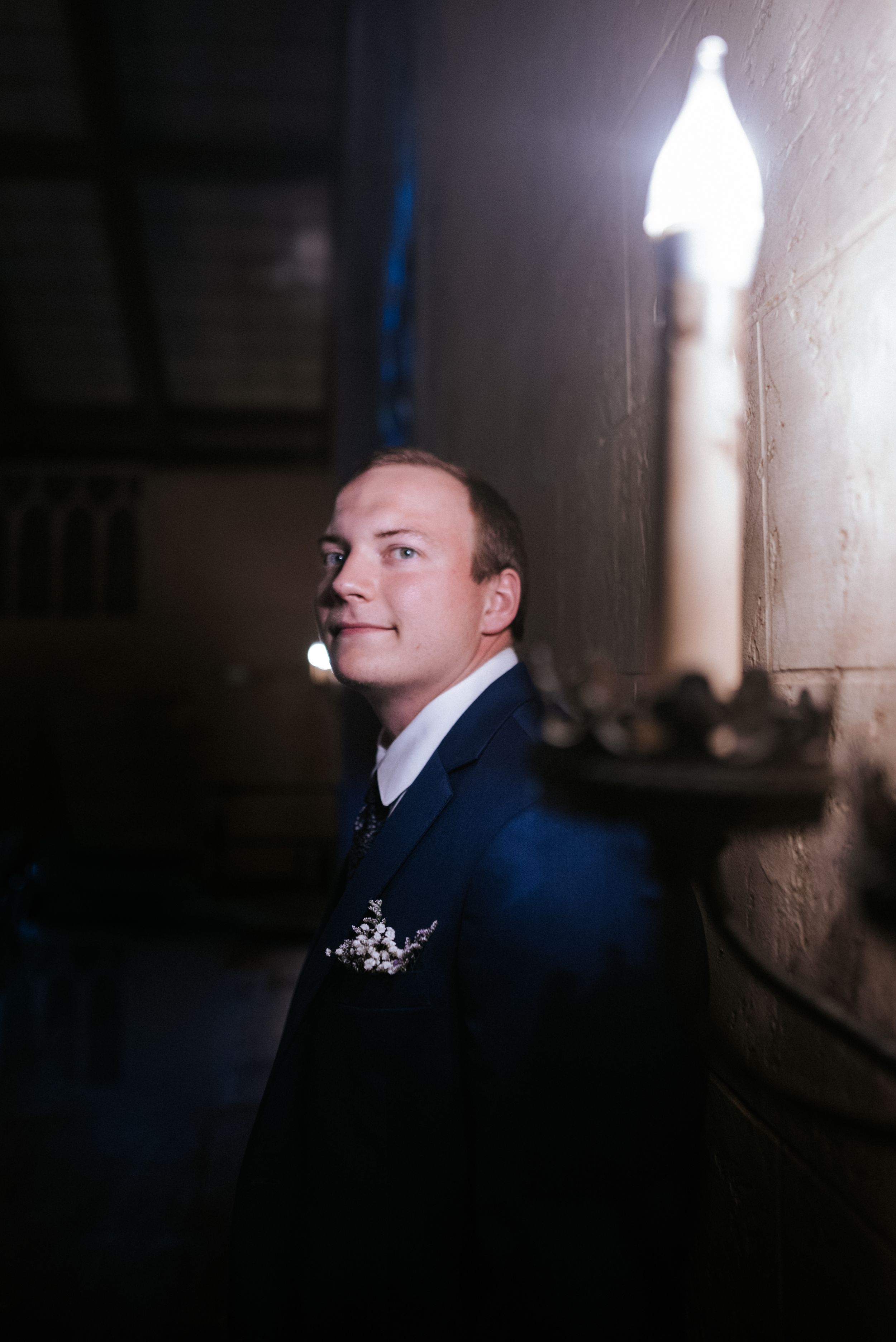 Groom portrait in navy suit captured in dramatic lighting against dark wall.
