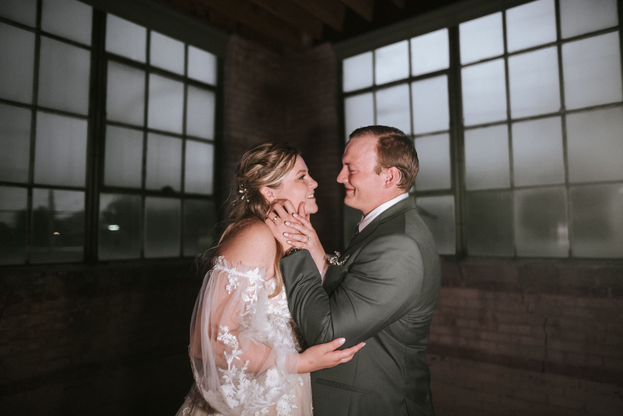 A tender moment between newlyweds sharing an intimate embrace in a sunlit room with window panels.