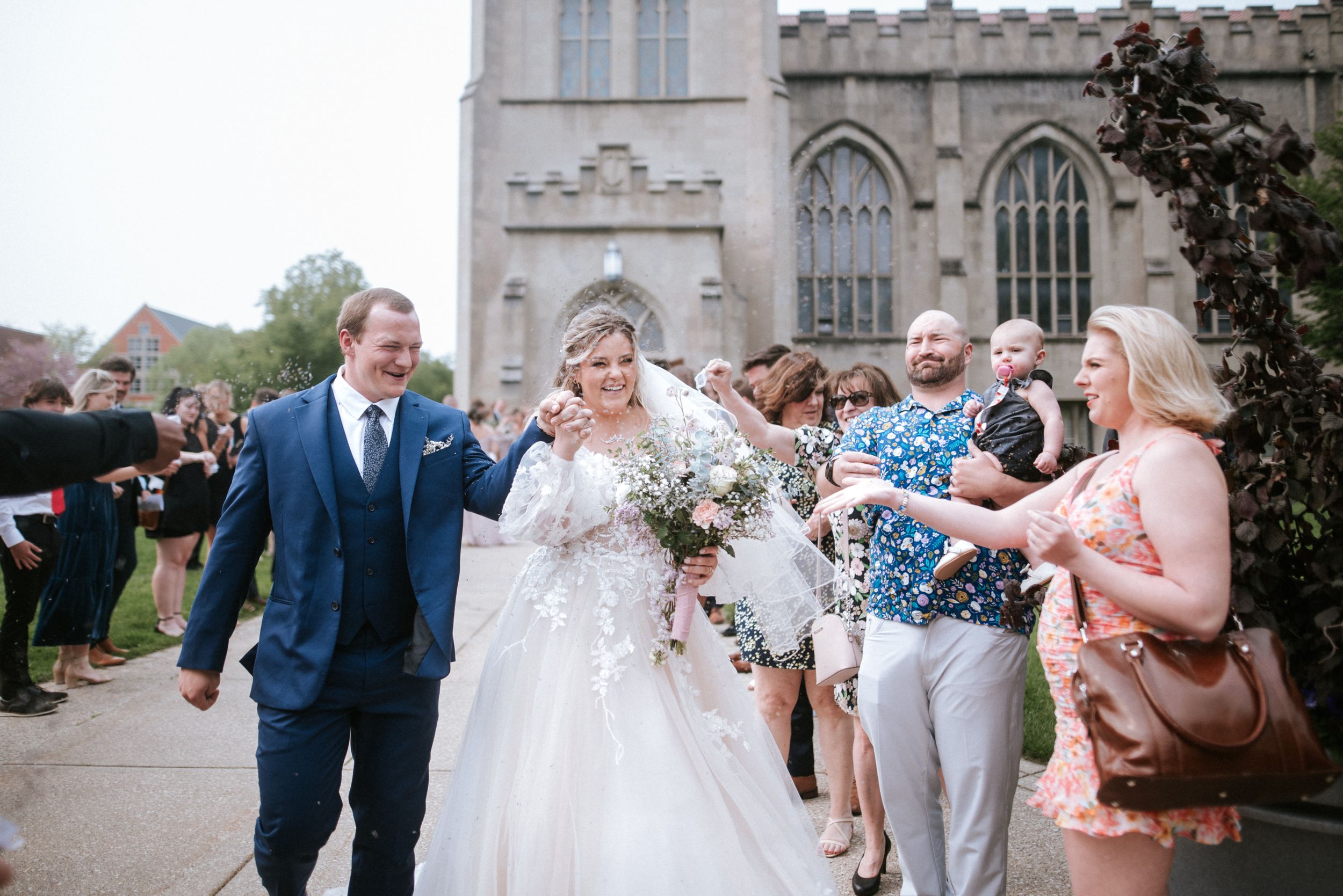 Wedding guests celebrate by tossing confetti at newlyweds outside gothic church.