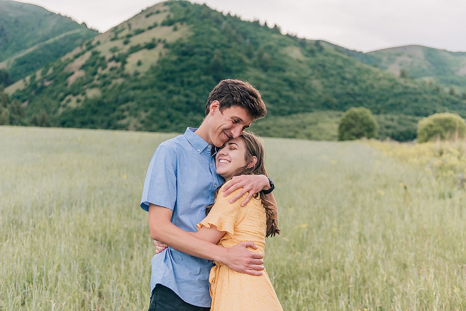 Intimate moment between couple in yellow dress and blue shirt in mountain meadow.