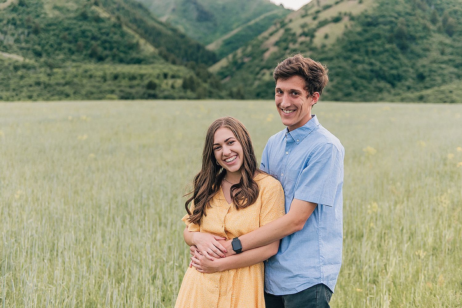 Sweet embrace captured in mountain meadow with dramatic peaks in background.