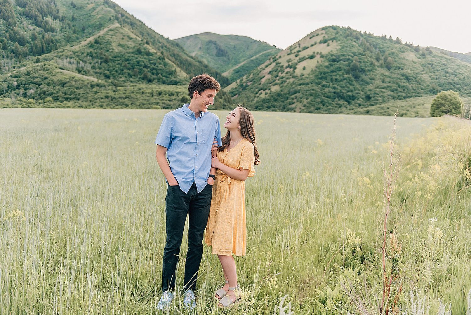Romantic outdoor portrait session in grassy field with mountain backdrop.