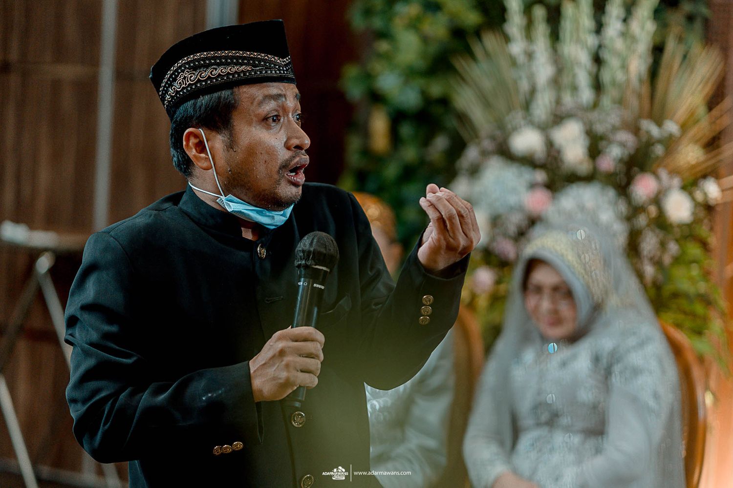 Religious official conducts traditional Indonesian wedding ceremony while holding microphone.