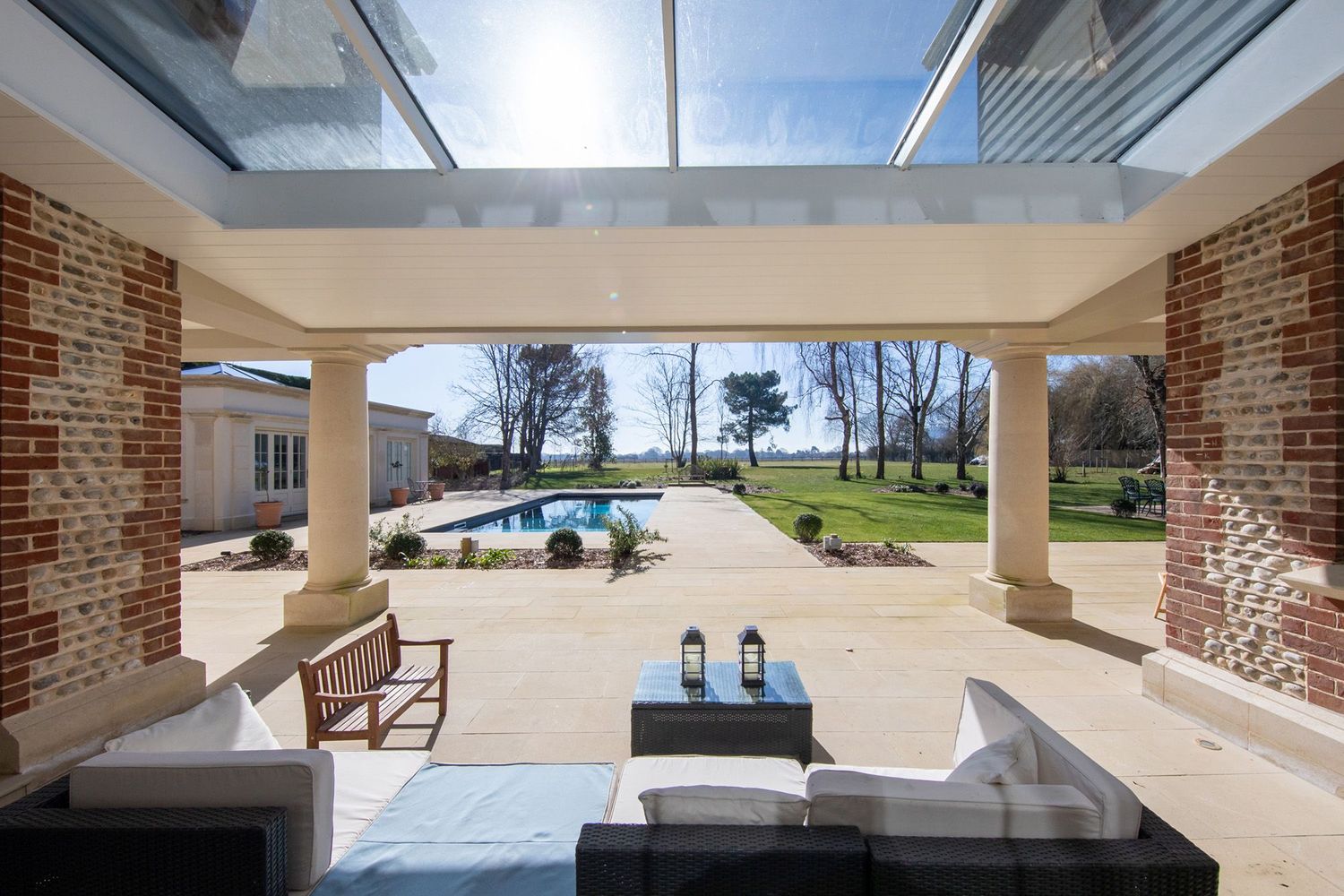 Covered patio with brick columns overlooking swimming pool and landscaped grounds.