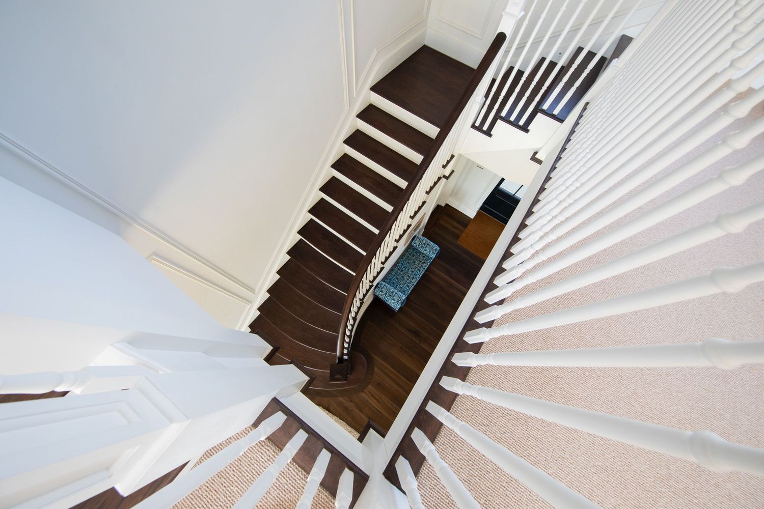 Modern spiral staircase with white railings and dark wood steps viewed from below.