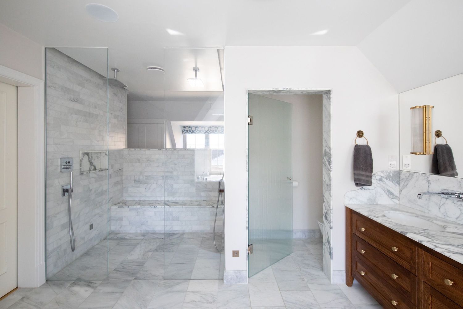 Modern bathroom interior with grey marble tiles, glass shower enclosure, and wooden vanity with white countertop.