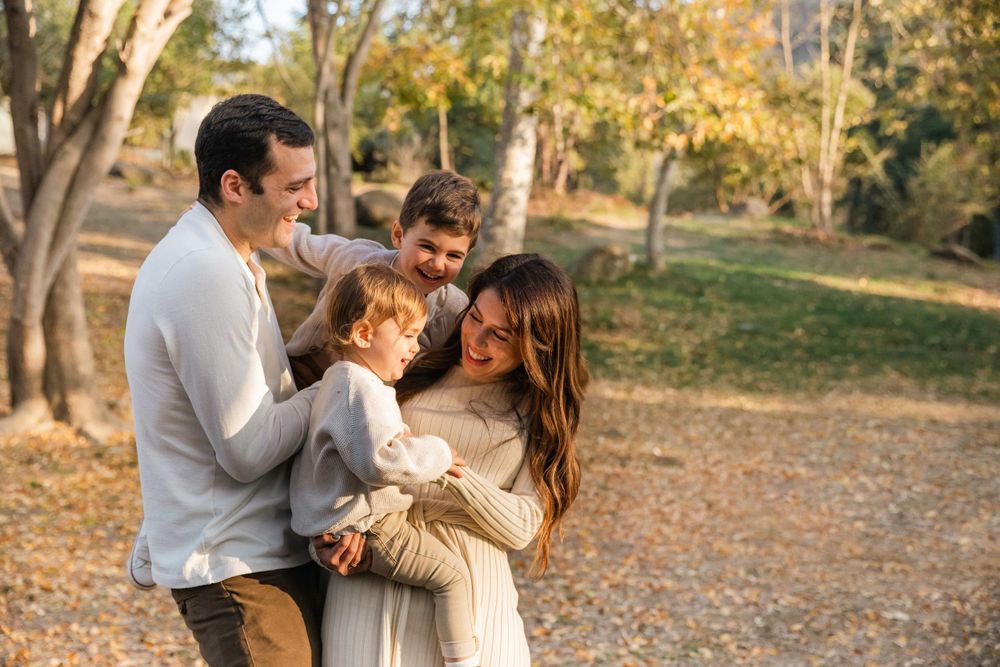 Loving family of four sharing a warm embrace among fall foliage in a sunlit park setting.