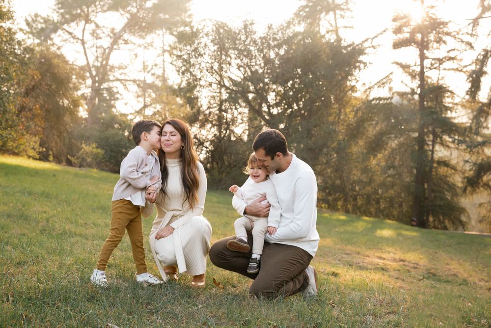 Family of four enjoying golden hour outdoors, mother and father sitting with two young children.